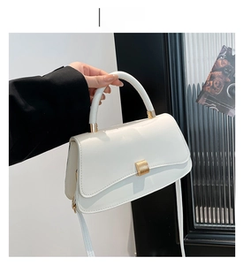 Detailed view of white leather crossbody bag with gold buckle and rigid top handle
