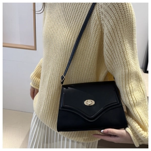 Close-up of a black minimalist leather crossbody bag featuring a gold oval twist lock closure