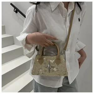 Dettaglio del ricamo floreale e del ciondolo a stella sulla borsa a mano in paglia