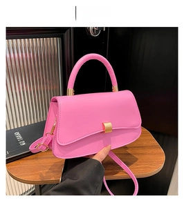 Detailed top view of a pink matte leather crossbody bag with a gold metal clasp on a wood table