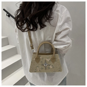 Detail of hand-woven straw bag featuring floral embroidery and a silver star charm