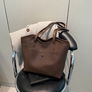 Brown faux leather tote bag with pocket on a chair next to an overcoat and a book
