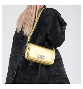 Detailed view of a metallic gold square bag with silver CD buckle on a black textured coat