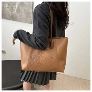 Detail of a large brown tote bag with snake pattern stitching and long shoulder straps