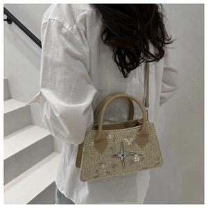 Detail of straw handbag featuring pink flower embroidery and a star metal buckle