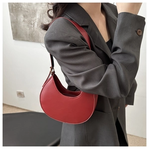 Macro view of a red crescent moon shoulder bag featuring matte leather texture and zipper