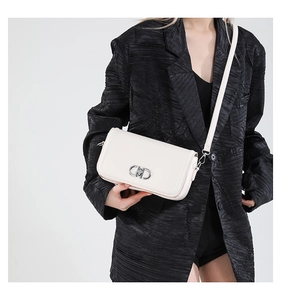 Close-up of minimalist cream-white crossbody bag with silver clasp on a black blazer