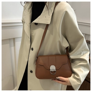 Detail of a brown leather crossbody bag with silver ring buckle on a beige trench coat