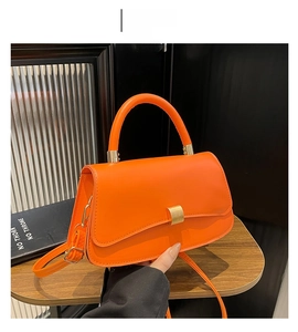 Detail view of a bright orange crossbody bag with gold rectangular buckle and handle