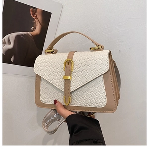 Detail of the woven leather texture and gold metal buckle on a two-tone crossbody bag