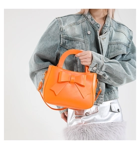 Close-up of vibrant orange bow handbag featuring gold hardware and premium PU texture