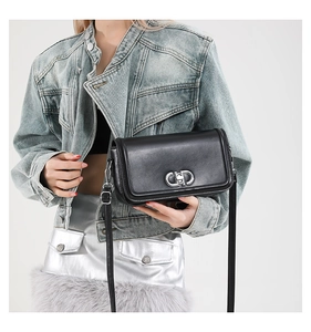 Detail of black leather crossbody bag with silver interlocking metal clasp and strap