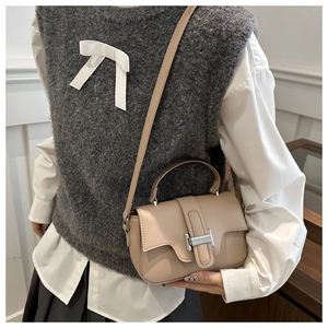 Close-up of minimalist beige leather crossbody bag with iconic silver H-shaped buckle