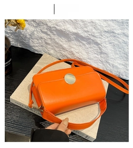 Vue détaillée du sac en cuir orange avec boucle ronde argentée et deux bandoulières
