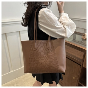 Detail of a brown tote bag featuring embossed crocodile pattern and smooth leather panels