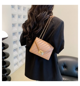 Detail of light brown quilted crossbody bag with gold chain strap shown on a model