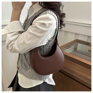 Close-up of a minimalist dark brown crescent shoulder bag worn with a white shirt