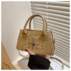 Dettaglio della borsa in paglia intrecciata con ricamo floreale e ciondolo a stella in metallo