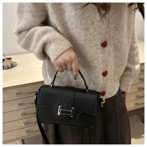 Black matte leather crossbody bag with silver buckle held by a model in a knit cardigan