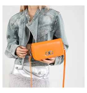 Detail of bright orange square crossbody bag with metallic silver buckle and leather strap