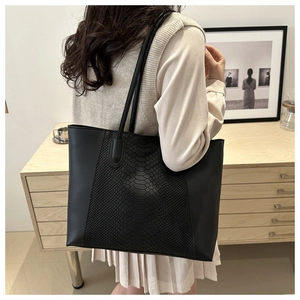 Detail of black tote bag showing crocodile texture contrast and long leather shoulder straps