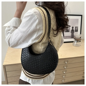 Detail of black faux crocodile leather crescent bag with golden hardware on a shoulder strap