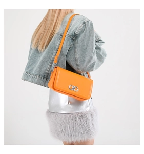Close-up of vibrant orange crossbody bag featuring a classic silver metal twist lock
