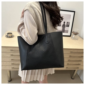 Detailed view of black crocodile pattern tote bag worn on shoulder by a model