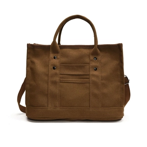 Borsa tote in tela marrone con rivetti in metallo e tracolla su sfondo bianco