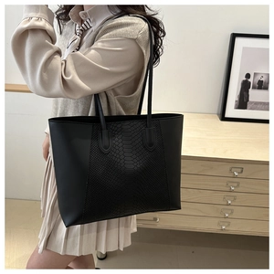 Detail of a large black tote bag with faux snake skin texture worn by a model