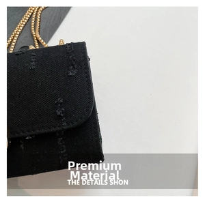 Detail of black denim texture and gold chain strap on stylish mini crossbody bag