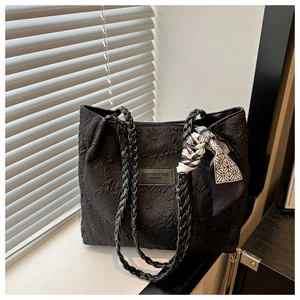 Detail of black textured tote bag featuring woven leather handles and printed silk scarf