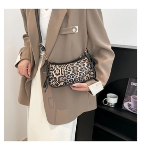 Chic leopard print shoulder bag with black trim and side ties on a tan blazer model