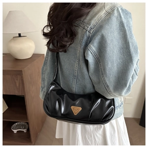 Close-up of black glossy pleated underarm bag with a triangular metal logo plaque