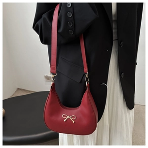 Detail of red crescent shoulder bag with golden bow and premium faux leather texture