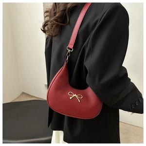 Detail of red hobo bag featuring a gold bow accessory and leather shoulder strap