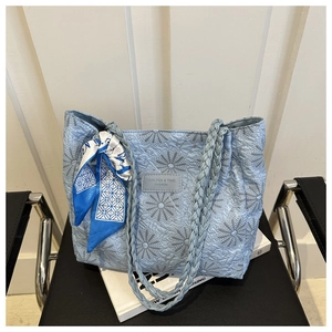 Detail of light blue quilted tote bag with daisy embroidery and woven handle with silk scarf