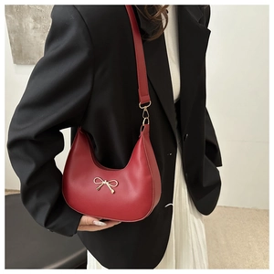 Detail of red leather hobo bag with gold bow clasp and shoulder strap on a model
