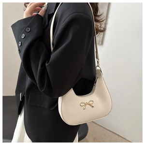 Detail of a creamy white crescent bag featuring a golden bow buckle worn by a model
