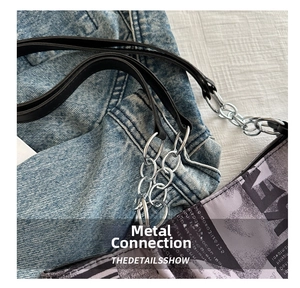 Detail view of silver metal chain link and black leather strap on a printed shoulder bag