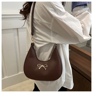 Detail of dark brown leather crescent bag featuring a delicate golden bow metal buckle