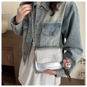 Detail of silver crossbody bag featuring happy cartoon bears and a plush bear charm