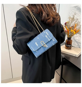 Detail of blue denim crossbody bag with gold U-shaped buckle and chain strap shown on model