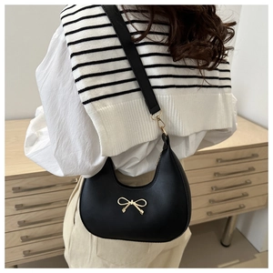 Detail of black hobo bag with golden bow hardware worn by a model in a minimal setting