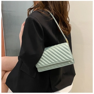 Sac bandoulière matelassé vert menthe porté sur un blazer noir style moderne