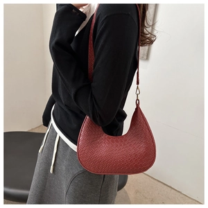 Model wearing a red woven crescent hobo bag with a gold buckle and shoulder strap
