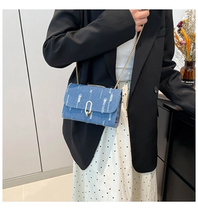 Close-up of distressed blue denim crossbody bag with gold metal buckle and chain strap