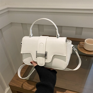 Minimalist white leather crossbody bag with silver metal buckle held in a cozy home setting