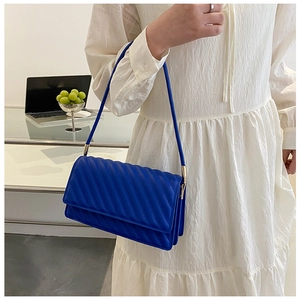 Détail du sac matelassé bleu foncé avec des finitions dorées sur une robe blanche chic