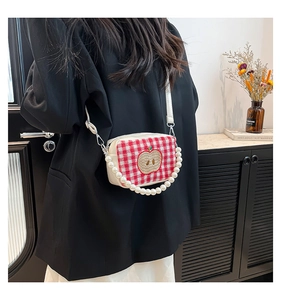 Detail of plaid crossbody bag with pearl handle and apple embroidery on a model